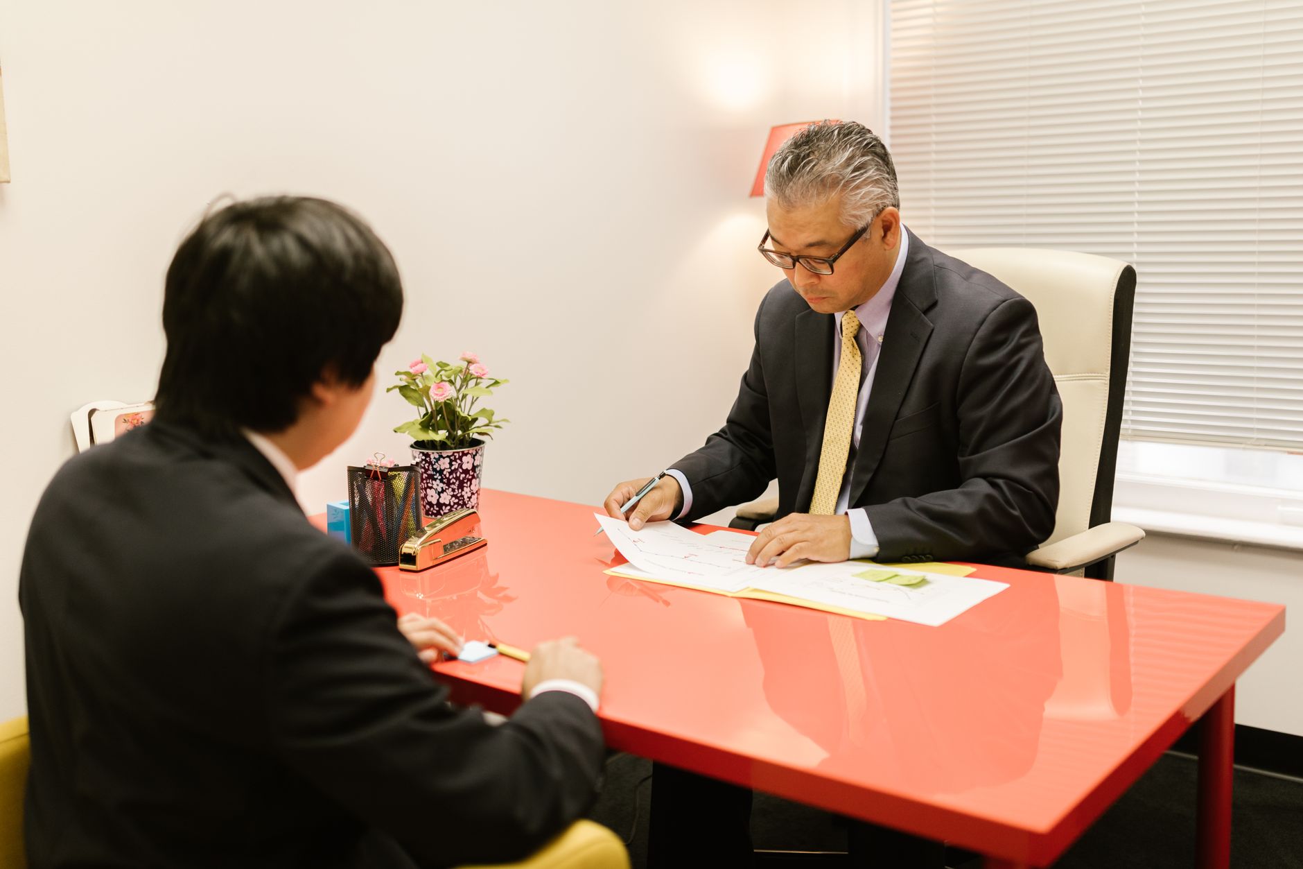 中小企業の経営者と発信担当者が、モニターを見ながら発信計画について穏やかに対話しているオフィスシーン。自然光が入る温かい雰囲気